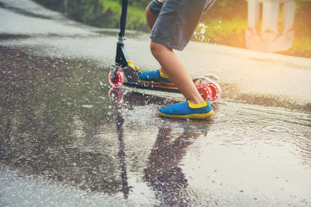 vintage tone image of asian boy playing scooter on wet ground .