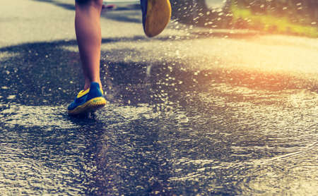vintage tone image of boy running on wet street after rain.(focus on ground)の写真素材