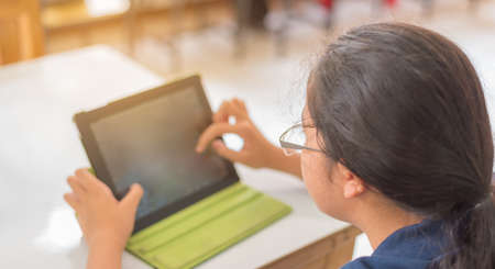 image of Asian cute girl touching on screen of tablet on table.の写真素材