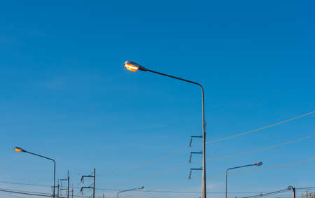 image of street lamp post with bright light bulb open on day time to waste energy.の写真素材