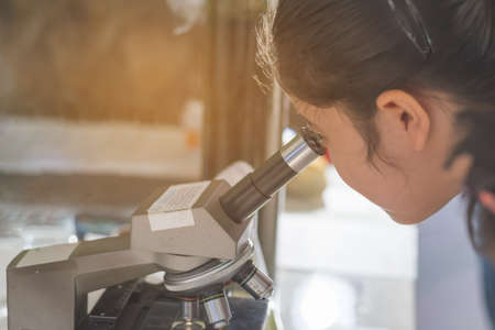 image of young asian girl use microscope to see small living thing at school laboratory.の写真素材