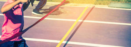 Close up image of red ribbon at finish line with kids winner crossing it.(vintahe tone)