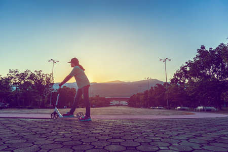 vintage tone silhouette image of Asian girl playing scooter on open space in park.の写真素材