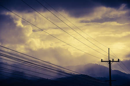 vintage tone image of high voltage electric wire on pole with cloudy sky and mountain before rain on evening time.の写真素材