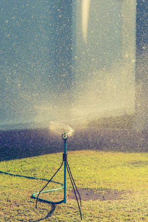 Vertical image of lawn sprinkler system with fine water droplets are sprayed out from the head machine reflecting to the morning sunlight.の写真素材