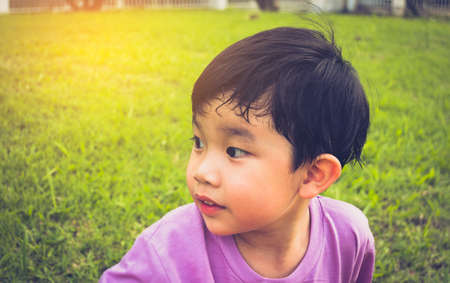 image of Young Asian boy looking on left side in park with green grass field in background.の写真素材