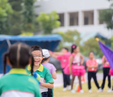 A smiling grumpy boy runs in the lawn during the competition, holding a green ballon ball in his school sports uniform.の写真素材