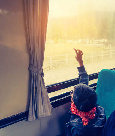 vintage tone image of Asian kid  sit on back seat in bus and look to outside with  hand drawing cartoon on water on window glass.の写真素材