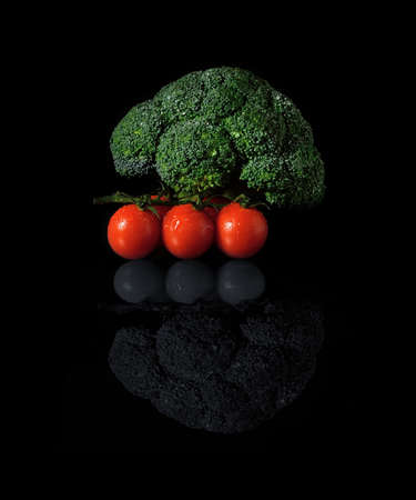 From my new series called Black Food  Close up of a fresh green broccoli head and dew covered ripe tomatoes on a reflective surface against a black background  Copy space の写真素材