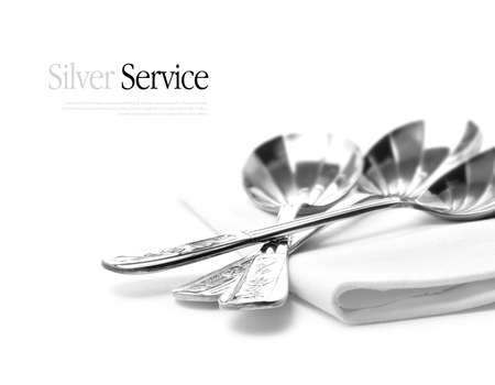 Macro image of sterling silver dessert spoons with subtle reflections on a folded napkin against a white background.の写真素材