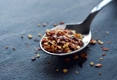 Close-up of crushed dried chilli flakes on a stainless steel spoon resting on a stone surface  Photographed in Mystic Light style  Copy space の写真素材