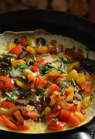 Delicious Spanish omellete cooking on a low heat with fresh chopped bell peppers, onions and chopped chives.の写真素材