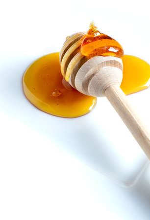 Bees honey flowing over  a wooden honey dipper stick isolated on a white porcelain plateの写真素材