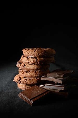 Luxury double chocolate chip cookies stacked with broken pieces of dark chocolate against a black background. Selective lighting. Copy space.の写真素材