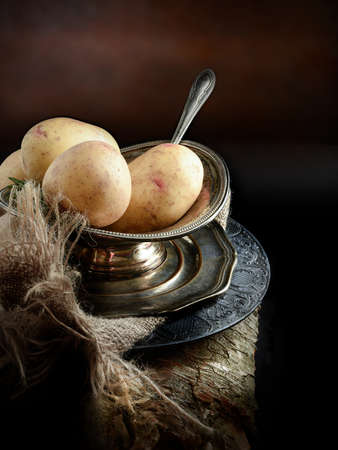 A curated image of fresh uncooked organic potatoes in an antique Victorian serving dish with hessian cloth against a dark, rustic background with copy space. Concept image for a restaurant menu cover design.の写真素材
