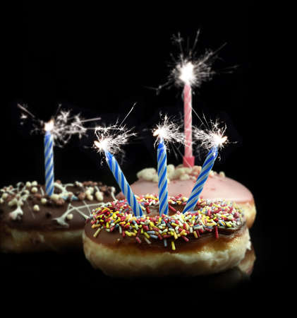 Creative image of delicious donuts with blue and pink candle sparklers against a black background with copy space. Concept image for celebrations or birthdays.の写真素材