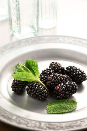 Fresh summer blackberries photographed in bright morning light with fresh mint sprigs against a light background with copy space.の写真素材