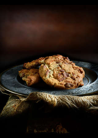 Home baked double chocolate chip cookies in a rustic, antique setting with creative lighting with generous copy space. Concept image for your dessert menu cover design.の写真素材
