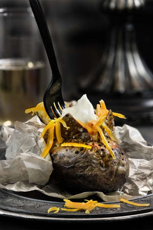Baked jacket potato with red grated cheese against a dark background. Generous accommodation for copy space. The perfect image for your lunch menu cover design.の写真素材