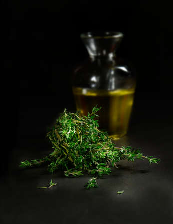 Creatively lit studio image of fresh thyme herb leaves against a dark background with a decanted glass flask of olive oil. Concept image for Italian cooking ingredients. Copy space.の写真素材