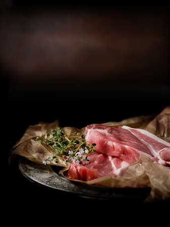 Uncooked, fresh pork fillets with thyme herbs against a dark, rustic background. Selective focus...