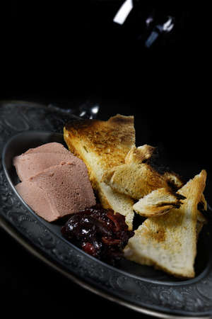 Creatively lit slices of Brussels pate with melba toast and pickled cherries. Concept image for a...