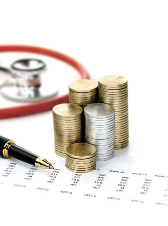Stethoscope, stacked coins, spread sheet and a pen against a light background with copy space. Concept image for soaring social care costs in the community.の写真素材
