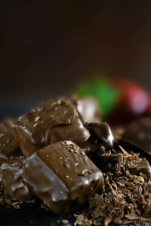 Creatively lit dark chocolate brownies with grated chocolate and strawberries against a dark...