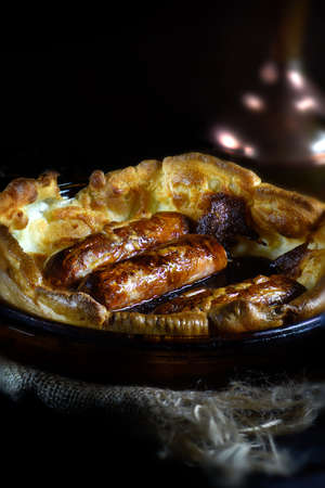 Pork sausages in Yorkshire pudding batter known as Toad In The Hole. Popular British dish when served with red wine onion gravy and steamed vegetables. Generous accommodation for copy space.の写真素材