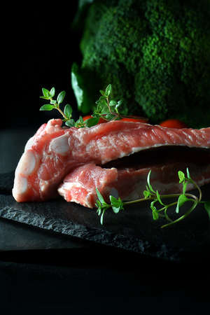 Uncooked prepared pork ribs with broccoli shot against a dark background with generous accommodation for copy space. Garnish with thyme herbsの写真素材