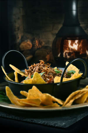 Bourbon Pulled Beef Brisket with crunchy nachos shot against a dark, rustic background with generous...