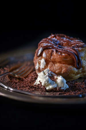 Creatively lit Belgium Chocolate Choux bun with fresh double cream and chocolate sprinkles shot against a dark background with generous accommodation for copy space.の写真素材