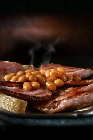 Close-up of delicious hot baked beans and smoky crispy pork bacon on fried toasted bread, shot against a creative, rustic background with generous accommodation for copy space.の写真素材