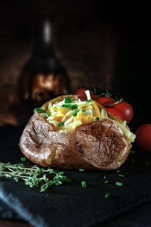 Four cheese baked potato with chives and thyme herbs shot against a rustic background with title and copy space. The perfect image for your restaurant or eatery menu cover design or point of sale display.の写真素材