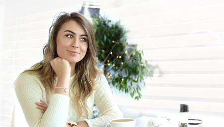 Beautiful young female student in a bright modern cafe smiling confidently while enjoying a cup of...