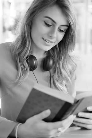 Beautiful young female university student studying in a coffee shop with headphones and reading a text book. Selective focus and rendered in greyscale. Concept image for university lifestyle.の写真素材