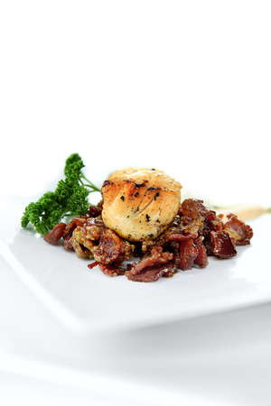 Seared scallops on warm smoked pork bacon with coral (roe) mousse with capers, Dijon mustard and parsley. Shot against a white background with generous accommodation for copy space.の写真素材