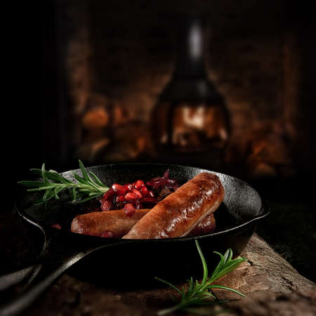 Grilled pork sausages with caramalized red onions and pomegranites in a wrought-iron black skillet shot against a dark background with accommodation for copy space.の写真素材