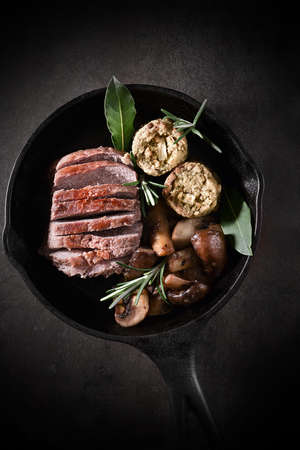 Pan fried in a wrought iron skillet roasted wild boar fillet with garlic mushrooms and sage, apple and onion stuffing balls with bay leaves and rosemary herb garnish.の写真素材