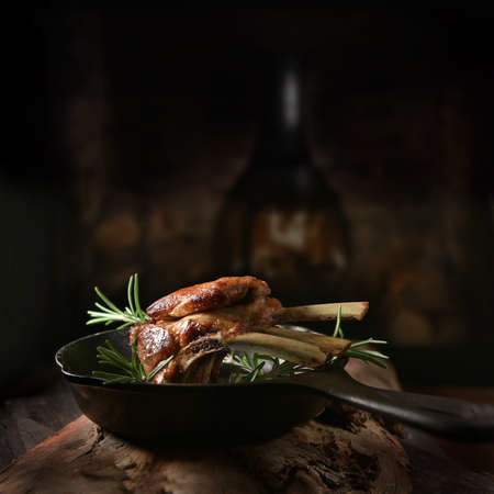 Traditional, roasted rack of lamb cutlets in a wrought iron skillet with rosemary herbs shot against a dark, rustic background with generous accommodation for copy space.の写真素材