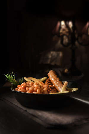 Traditional English fayre, grilled pork sausages, baked beans and chips, served in a wrought iron skillet shot against a rustic background. Generous accommodation for copy space.の写真素材