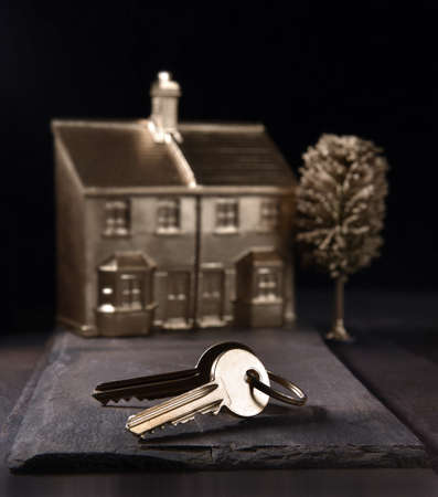 Concept image for new home ownership, purchase. Gold keys and house in background with accommodation for copy space.の写真素材