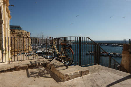 Bicycle parked on the shore of the harbor on a beautiful sunny day in Gallipoli - Salento - Italy