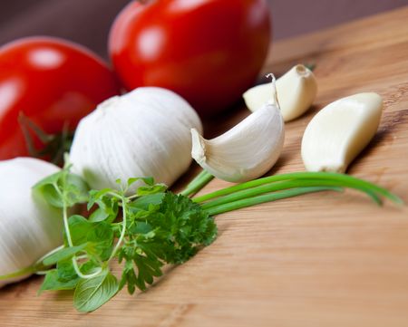 garlic and herbs on table with tomato in backgroundの写真素材
