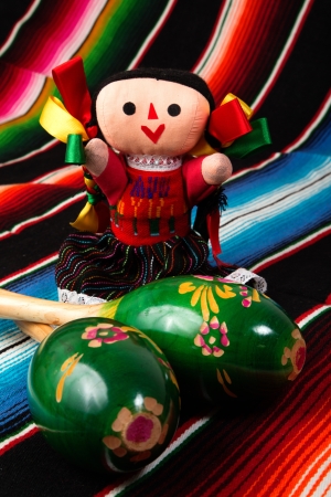 Mexican culture, beautiful traditional doll with maracas on a colorful serape blanketの写真素材