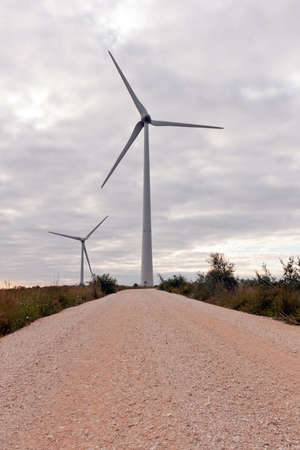 Gravel Road to a pair of Wind Turbines against cloudy skyの写真素材