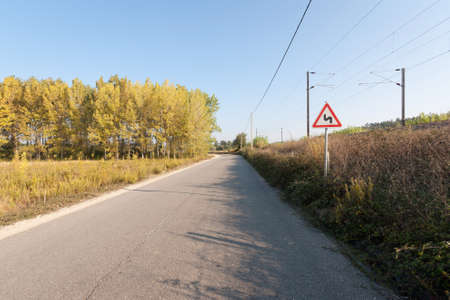 Road trough woods against blue sky with danger warning signalの写真素材