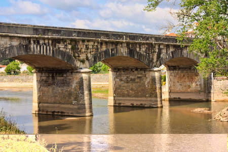 Old stone bridge over portuguese river against sky and cloudsの写真素材