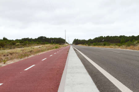 Roadside Red cycle path against forest and cloud sky の写真素材