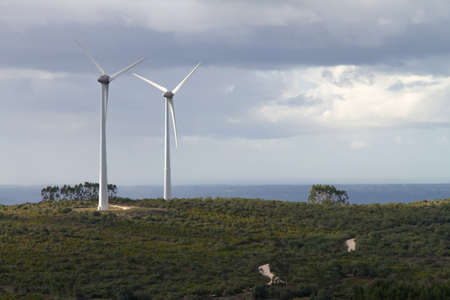 An pair of windmills turbines on the top of an hill